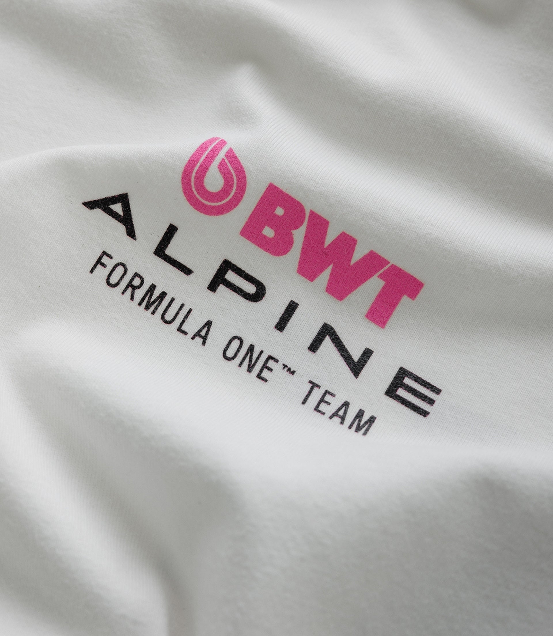 Close up of white fabric showing a pink BWT Alpine emblem and partial black lettering.