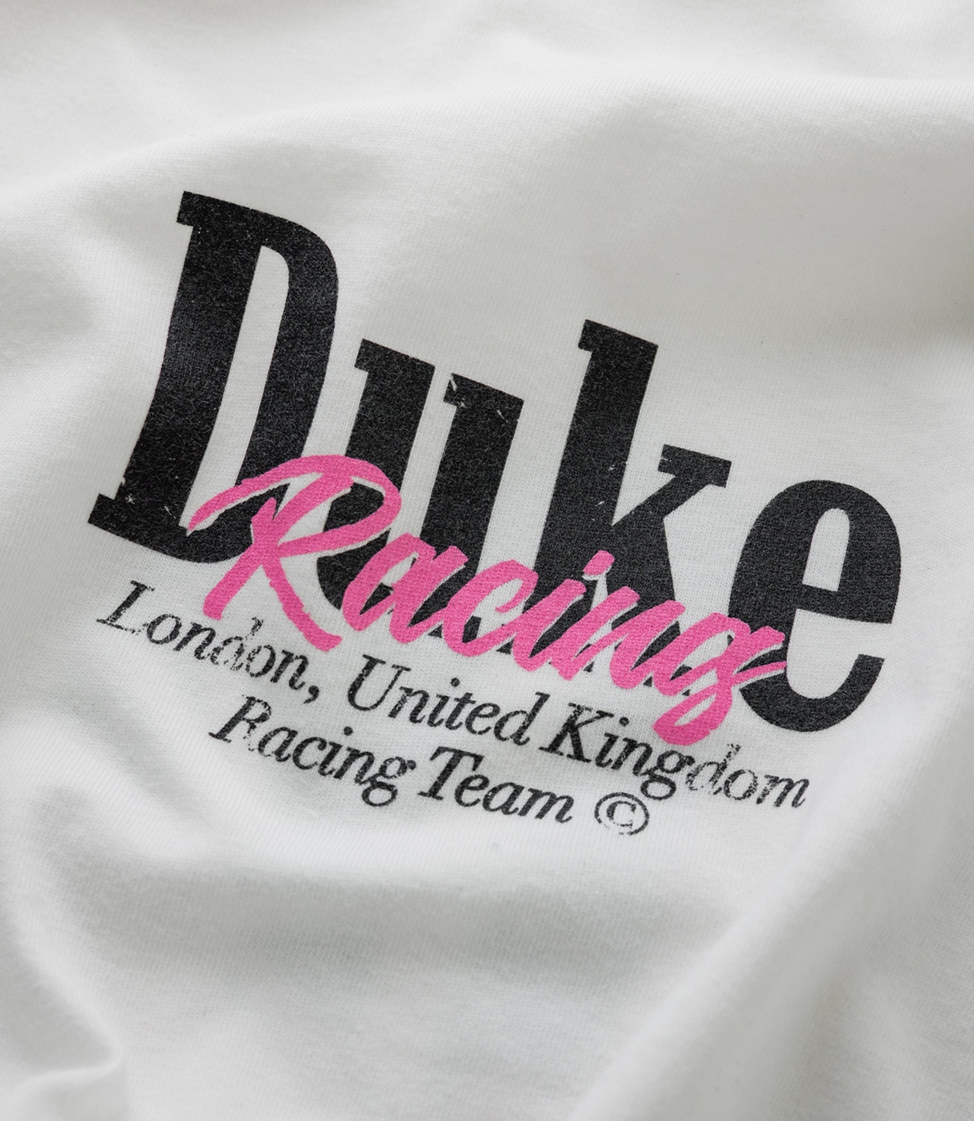 Close up of white fabric with bold black Duke lettering and bright pink Racing script across the print.
