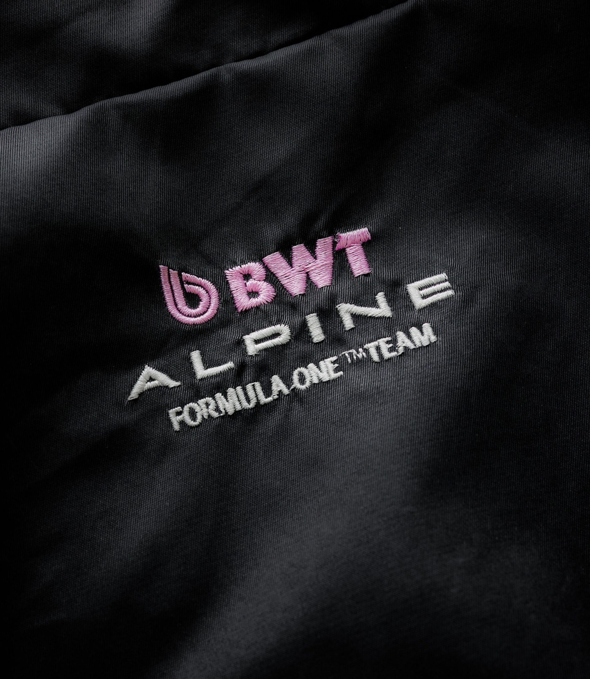 Close-up of black fabric showing pink BWT Alpine embroidery and white Duke & Dexter branding on the jacket