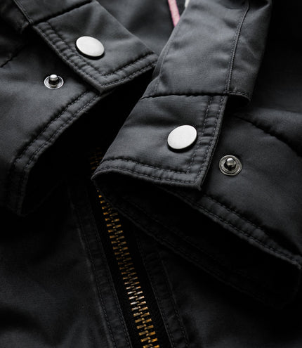 Close up of black trackside jacket showing metal snap buttons and heavy stitching