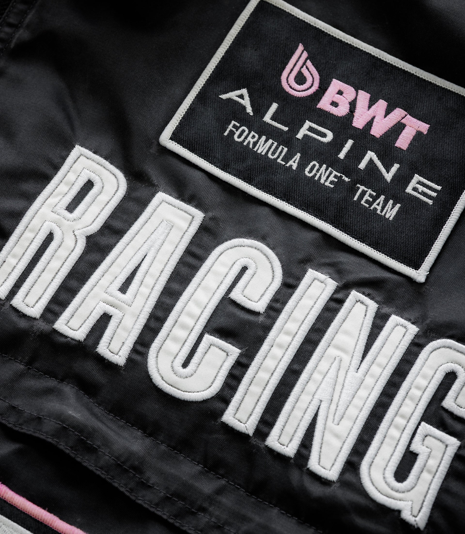 Close up of black jacket showing the pink BWT Alpine patch and white Alpine Formula One Team embroidery.