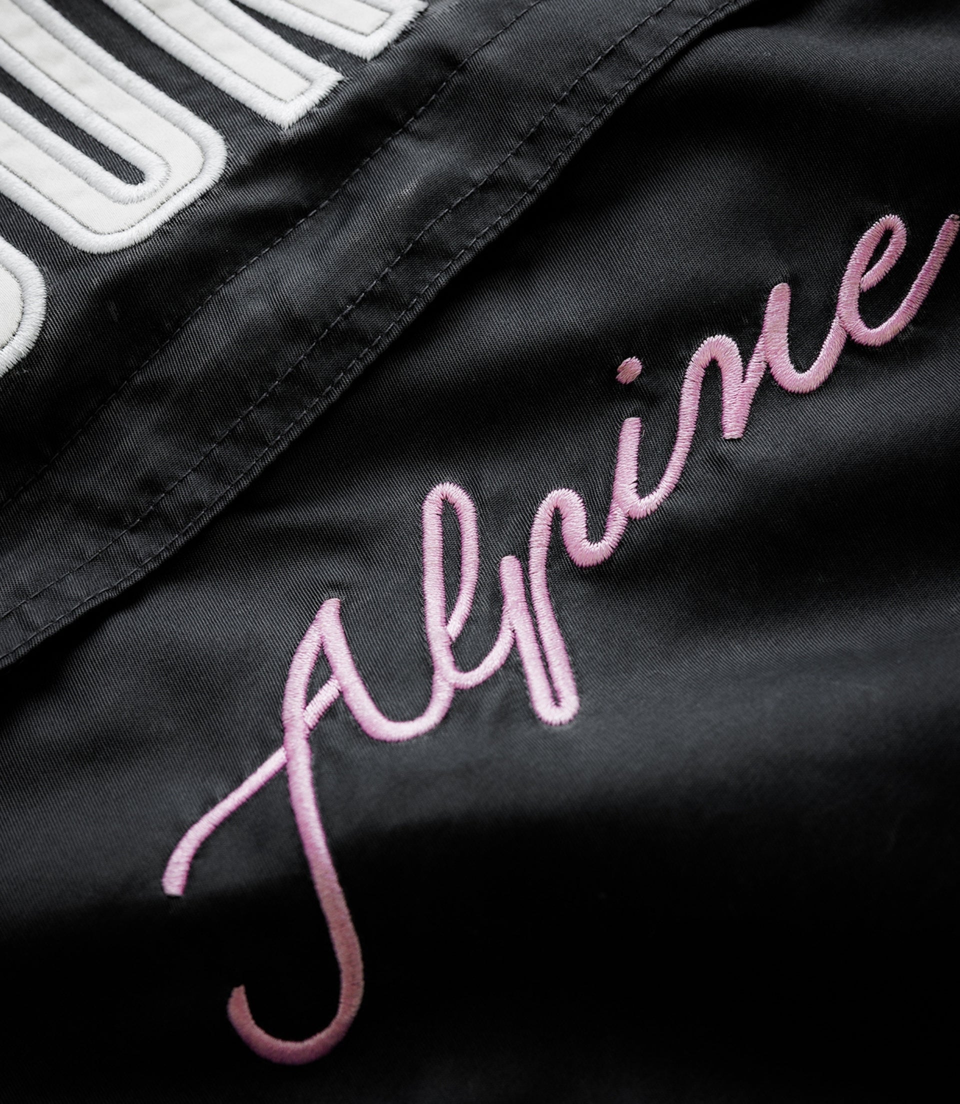Close up of black jacket fabric with white embroidery and pink script logo on the Duke & Dexter trackside design