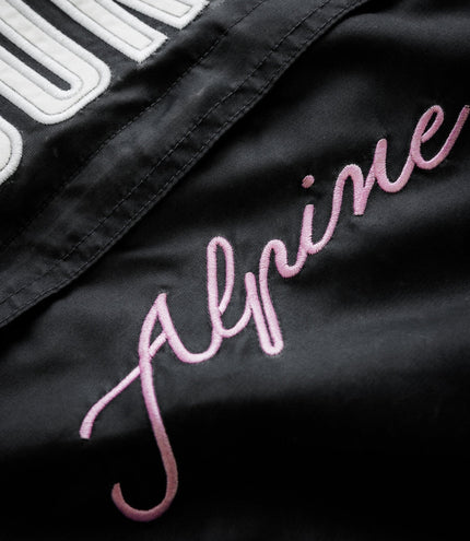 Close up of black jacket fabric with white embroidery and pink script logo on the Duke & Dexter trackside design