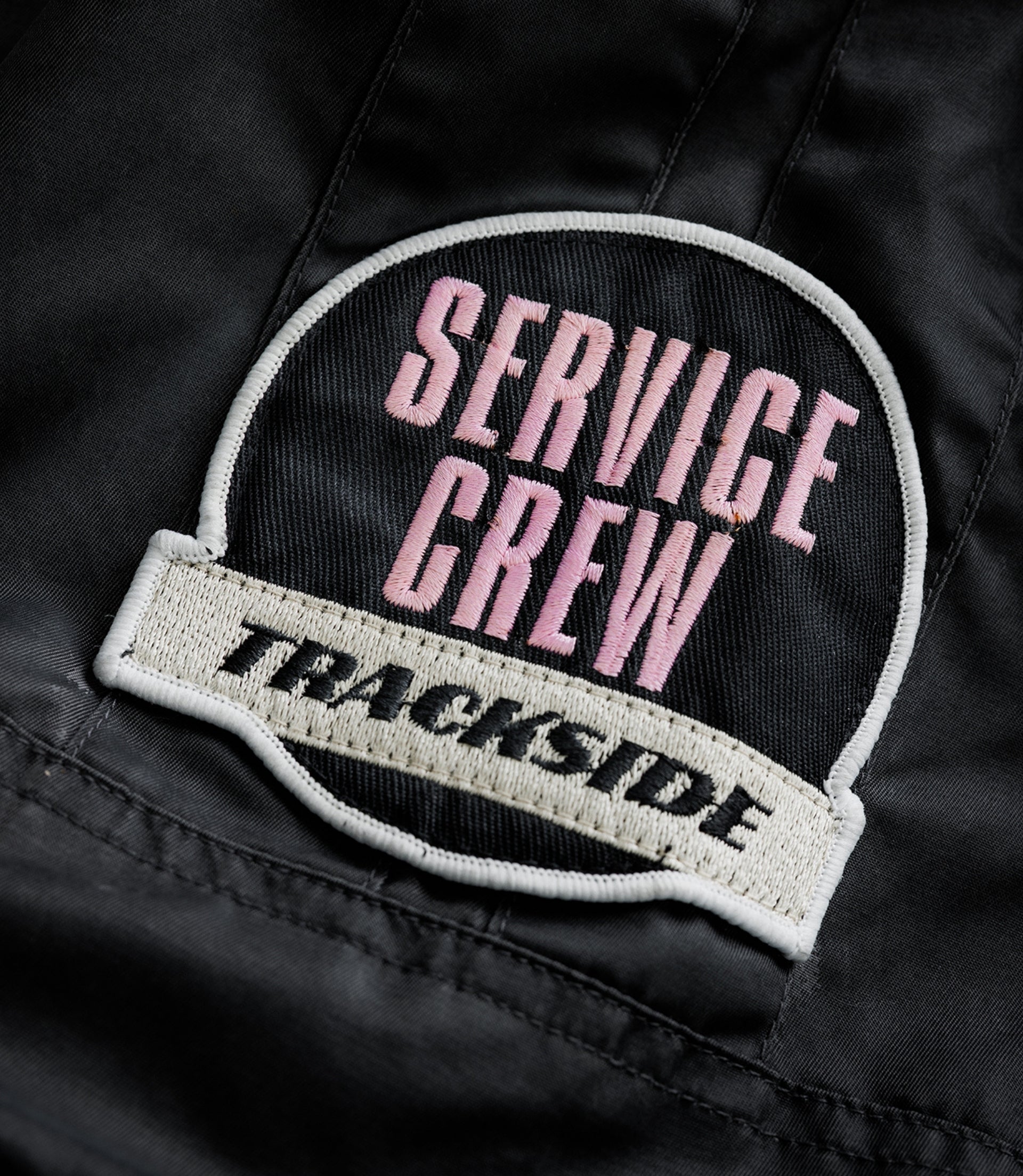Round embroidered patch with pink text on black fabric