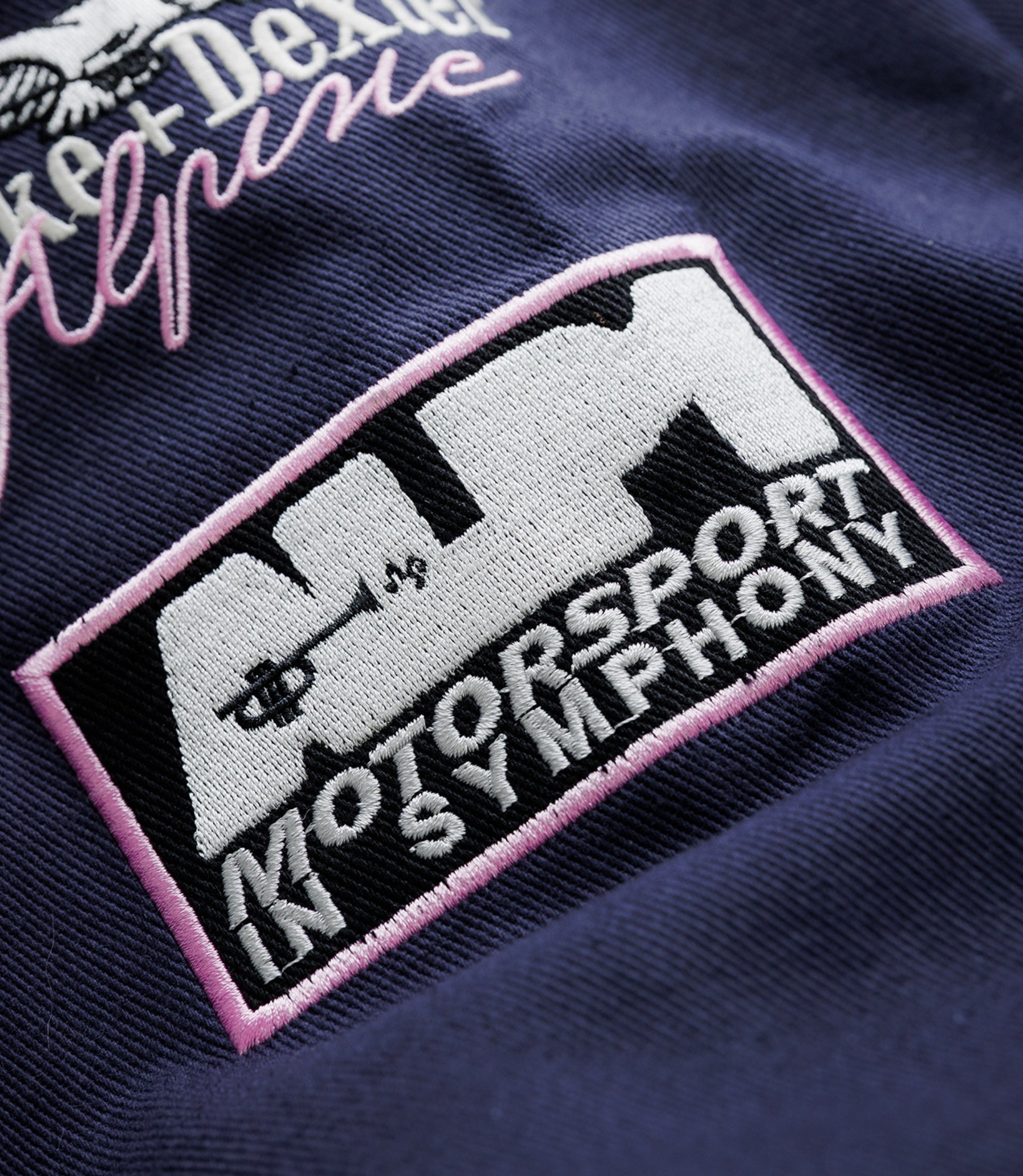 Close up of navy jacket sleeve with an embroidered crest and large white lettering on textured fabric