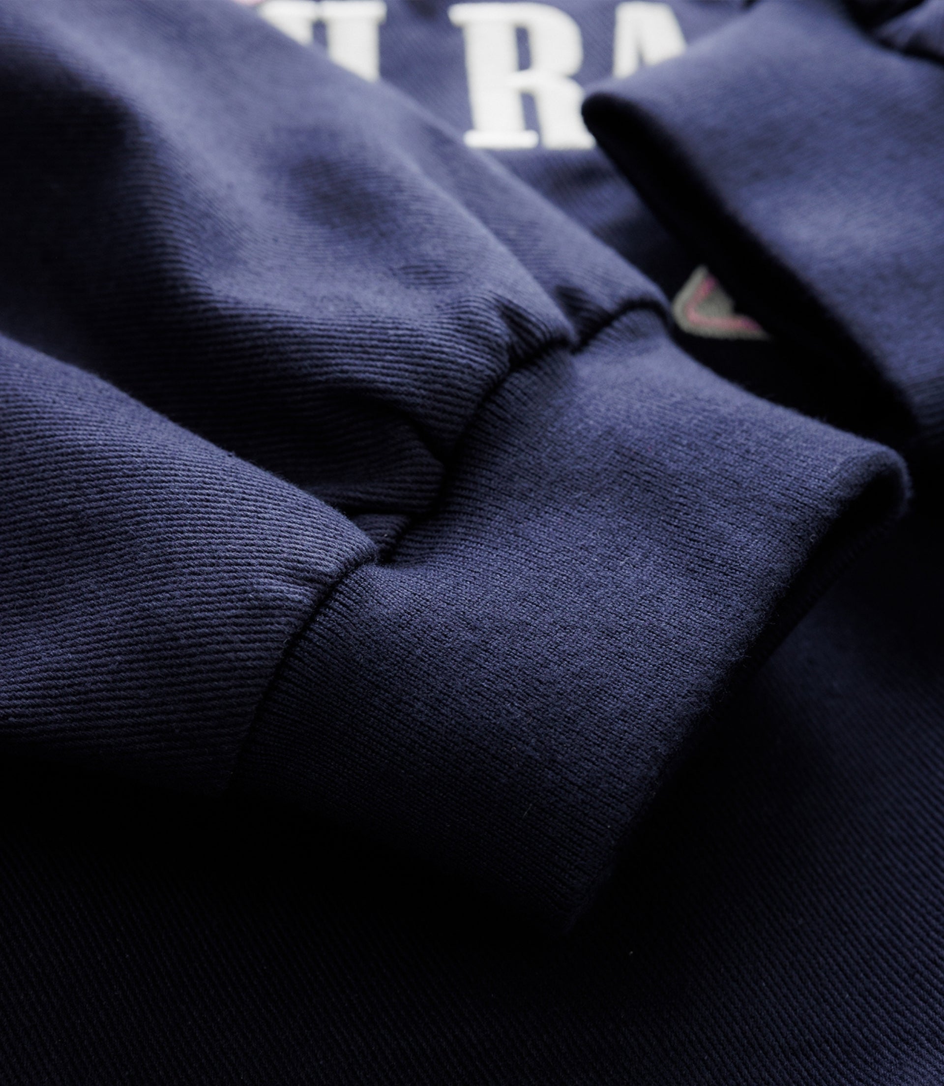 Close up of navy fabric with partial white block text and a small triangular patch near the seam