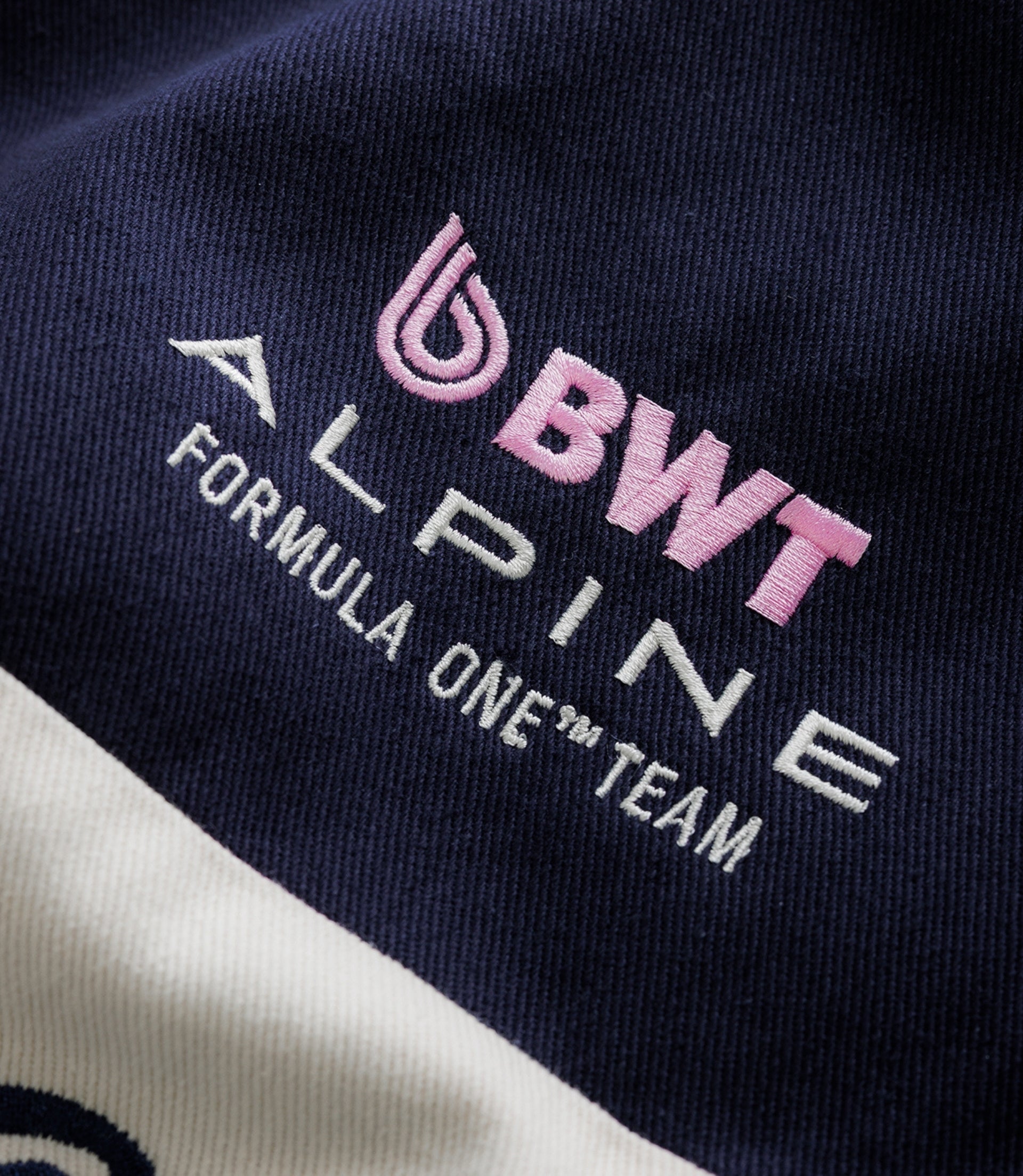 Close-up of pink Duke embroidery on navy fabric with partial crest and white stitching