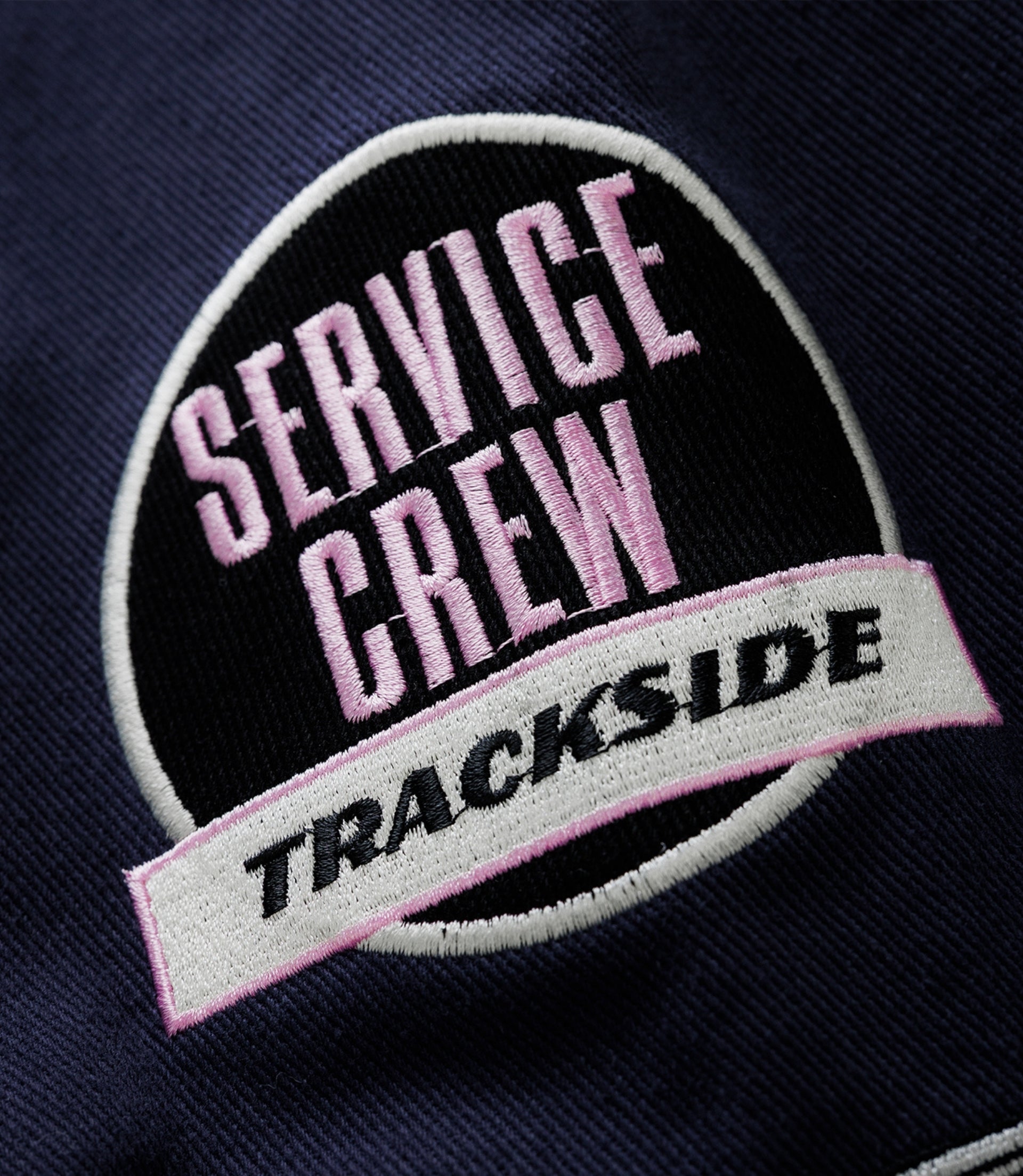 Close up of navy fabric with a round embroidered patch showing pink Alpine lettering and a white border