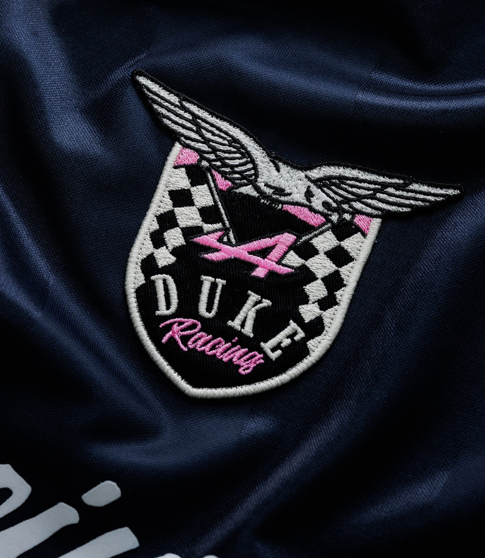 Close up of embroidered Duke Racing crest with pink detailing on navy fabric