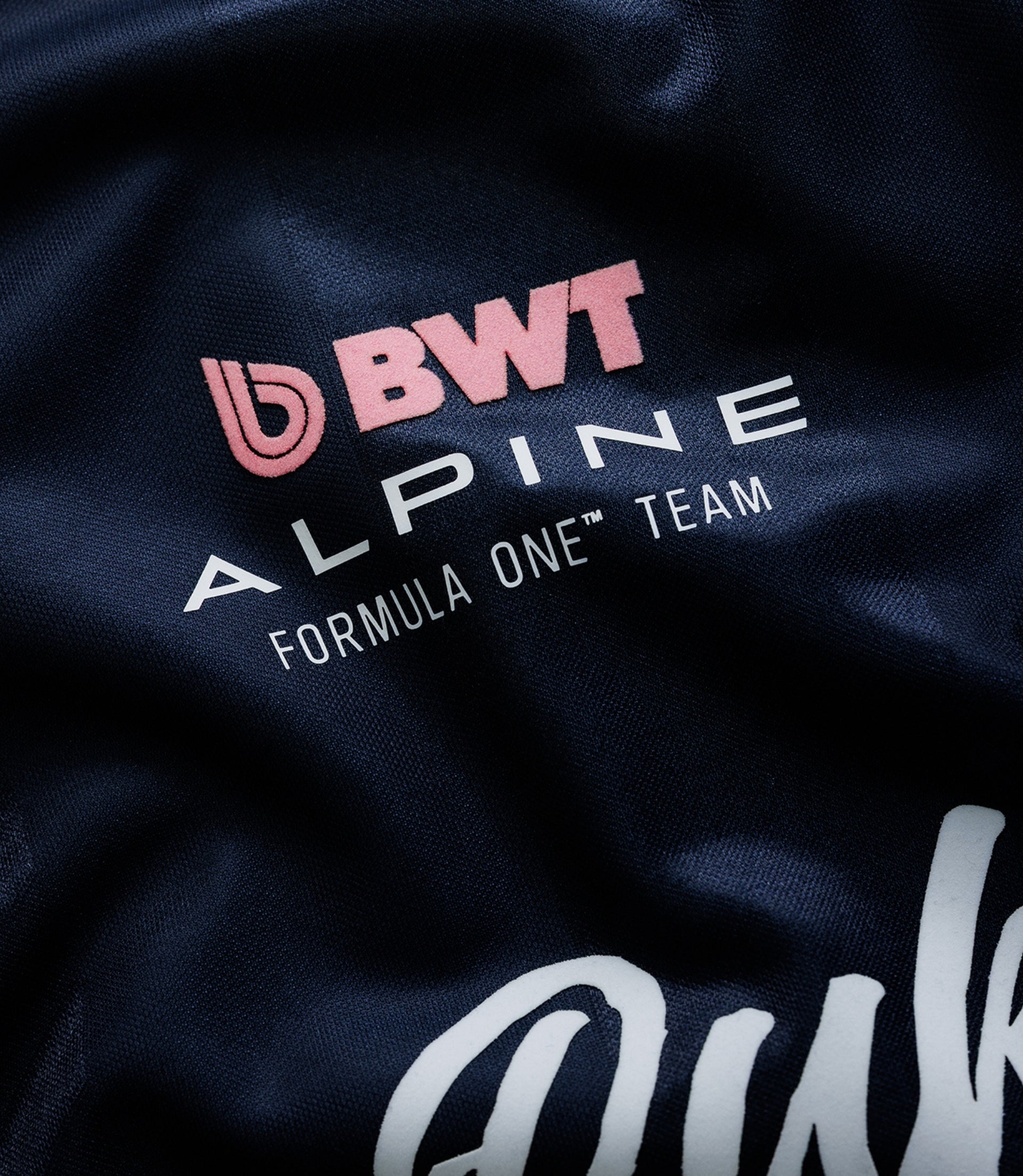 Close up of dark blue fabric with pink BWT Alpine logo embroidery on a Formula One team jersey