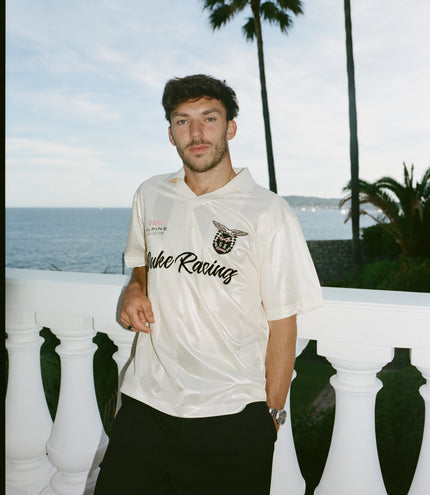 Man wearing a white Duke & Dexter Alpine racing jersey outdoors by the sea with palm trees