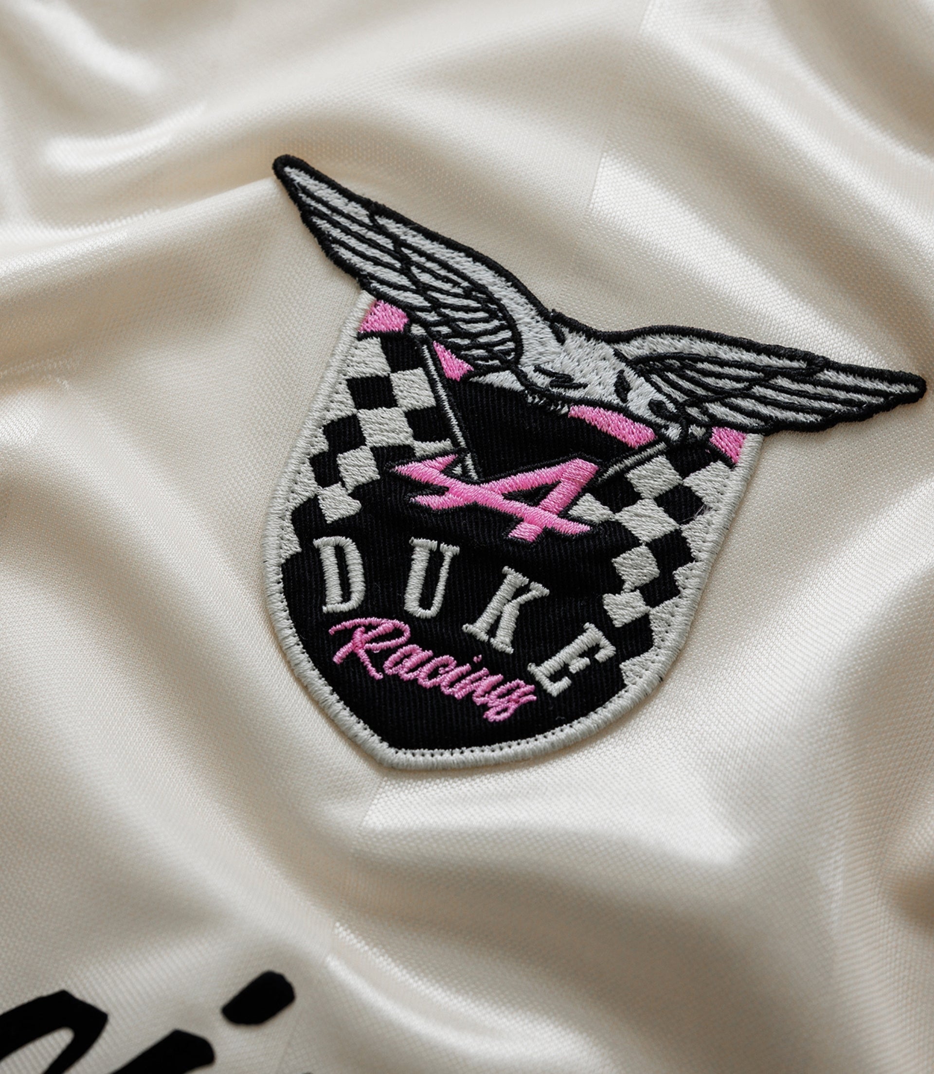 Close up of embroidered Duke Racing patch with wings and checkered design on satin fabric
