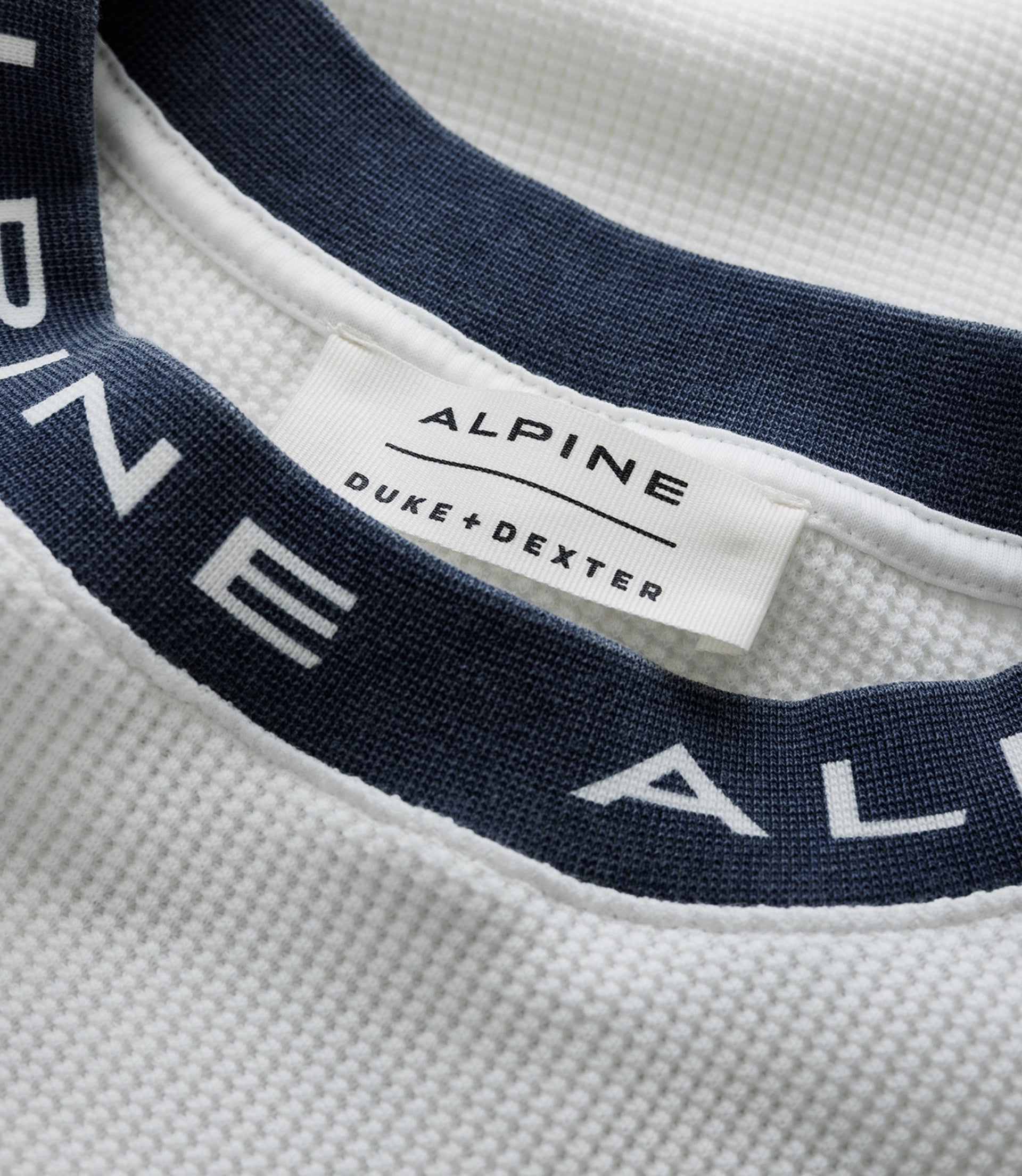 Close up of white waffle fabric with a navy Duke & Dexter strap and an Alpine label