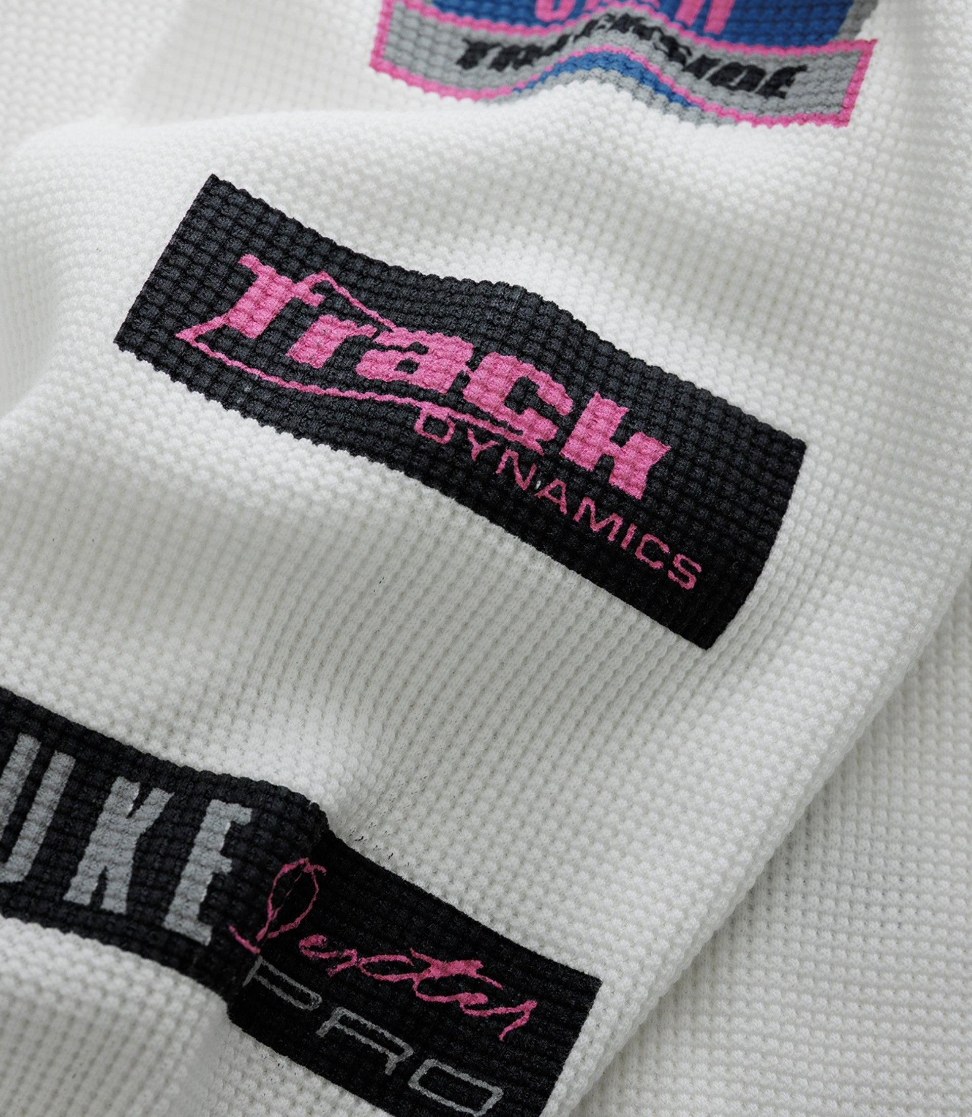 Close up of white waffle fabric showing a circular blue Alpine patch with pink text and a black Duke & Dexter label