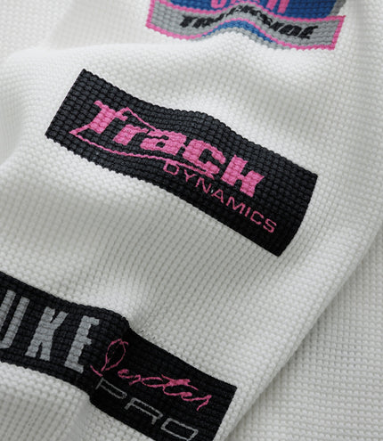 Close up of white waffle fabric showing a circular blue Alpine patch with pink text and a black Duke & Dexter label