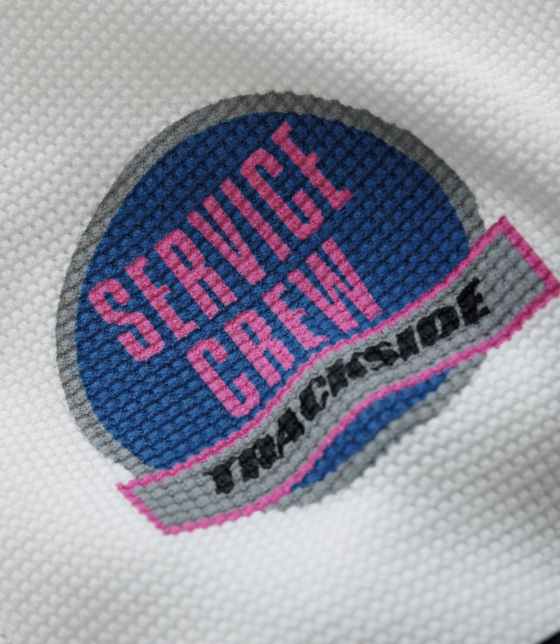 Close up of white waffle fabric featuring a blue Alpine patch and a pink Duke & Dexter label on black background