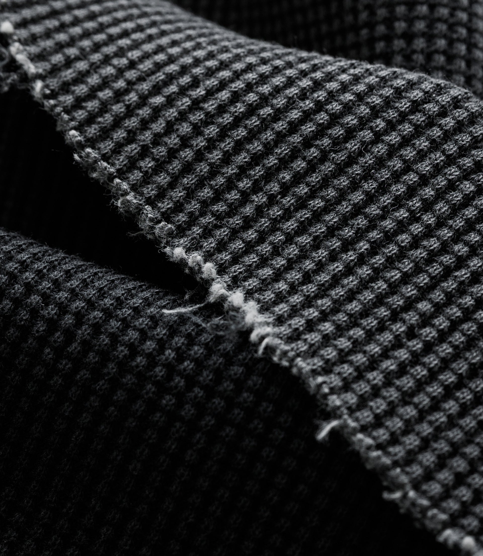 Macro shot of dark gray woven knit fabric showing a chunky waffle texture