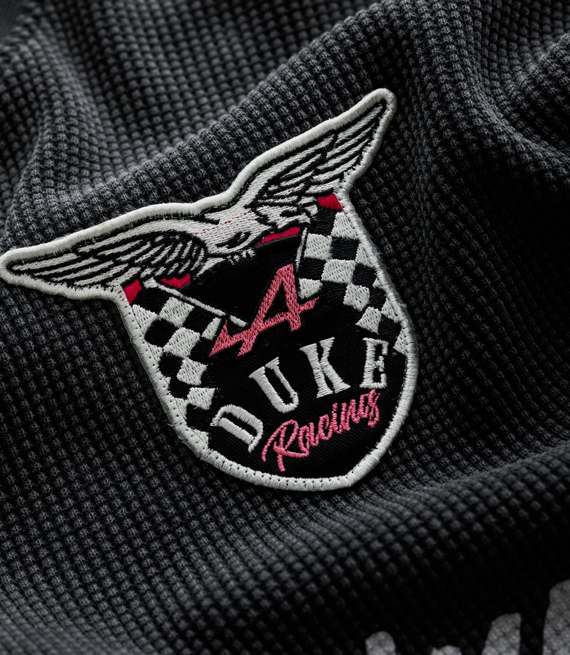 Close up of embroidered patch on dark knit fabric featuring wings and a checkerboard crest