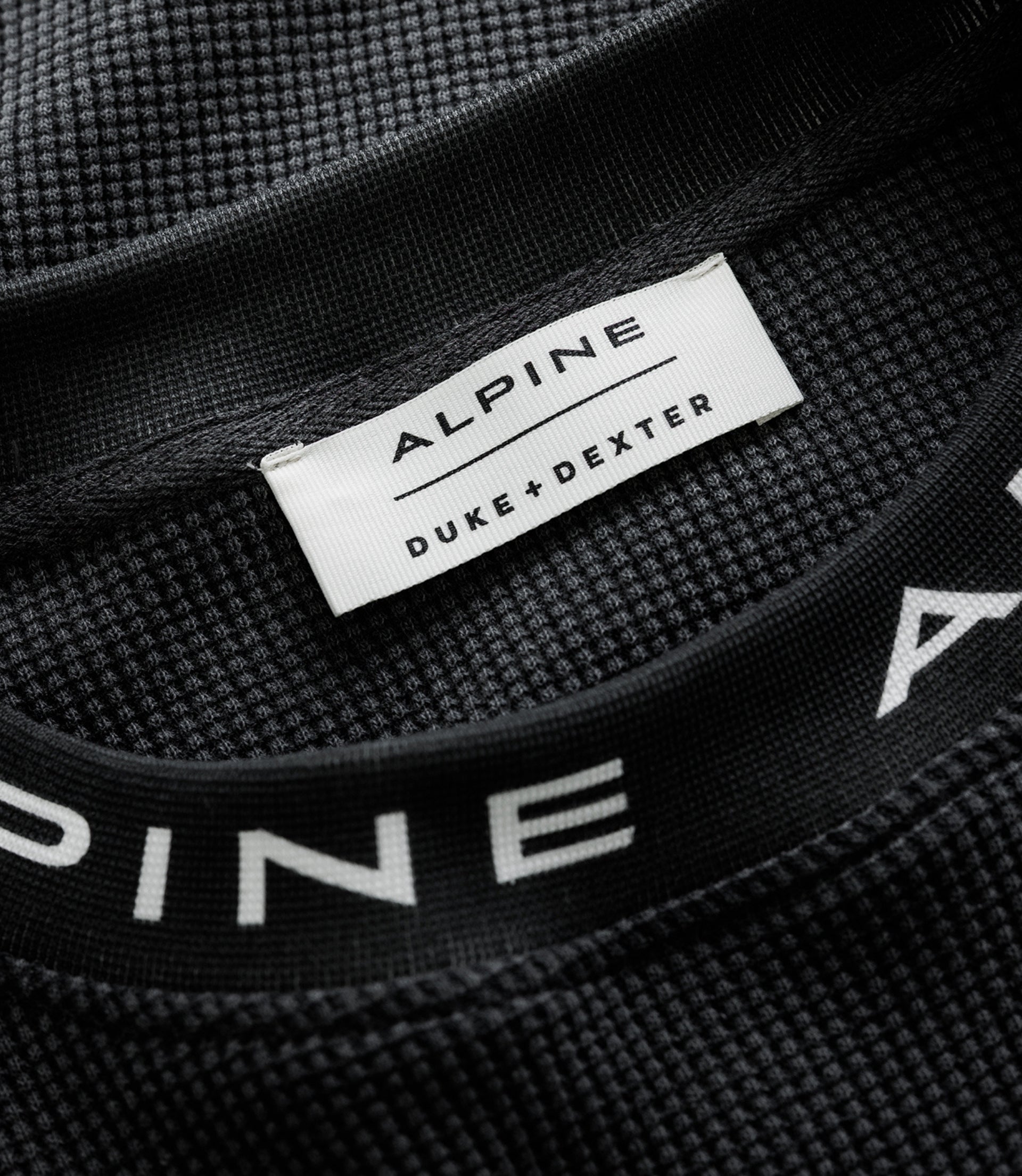 White tag reading ALPINE DUKE & DEXTER sewn into black jersey.