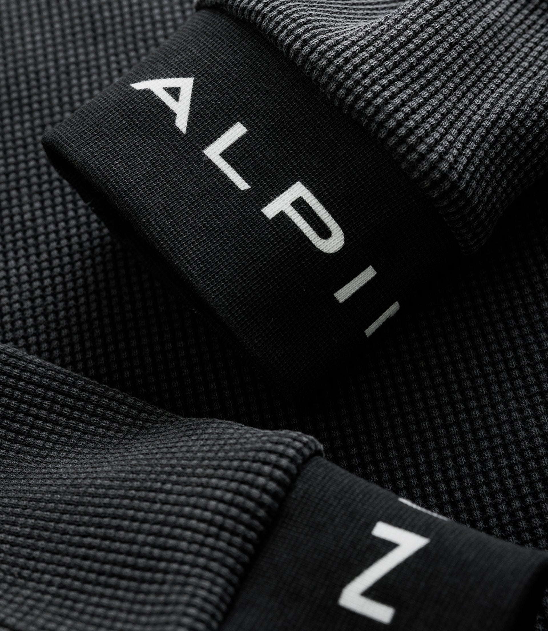 Close-up of black ribbed sleeve cuff with white Alpine logo on the jersey